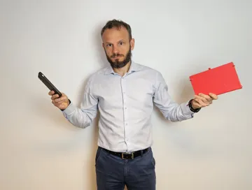 Piotr Szanser trzyma w jednej ręce smartfon, w drugiej tablet: który sprzęt i który program wybrać do spisu