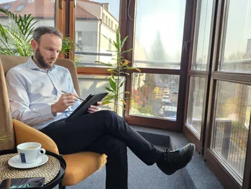 Piotr Szanser notuje rysikiem na tablecie, siedząc w fotelu przy oknie: spisywanie wymagań przed wyborem systemu